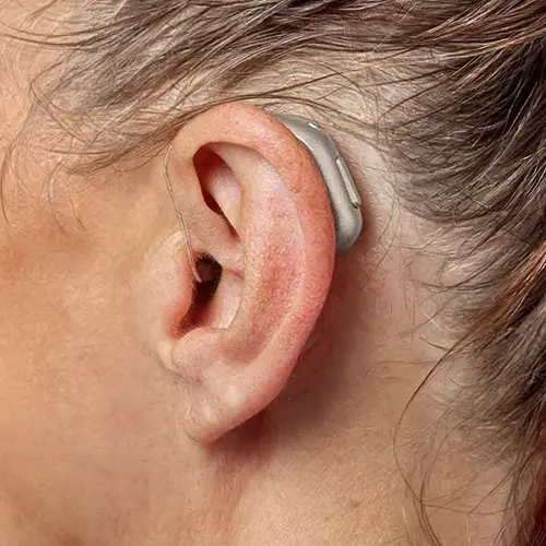 Typical high-street behind-the-ear hearing aid, flesh-toned, worn on an ear